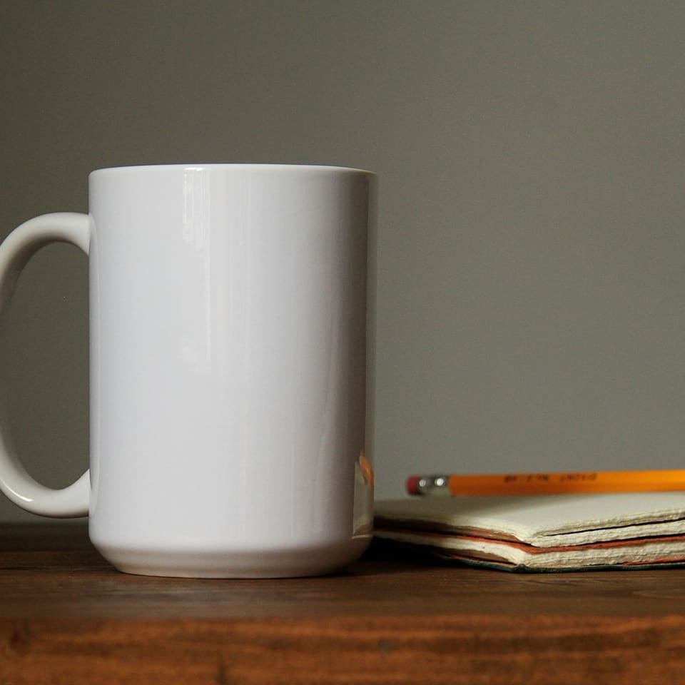 A plain white mug beside a notebook