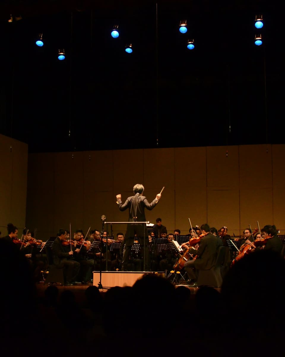 An orchestra and conductor performing on a dimly lit stage