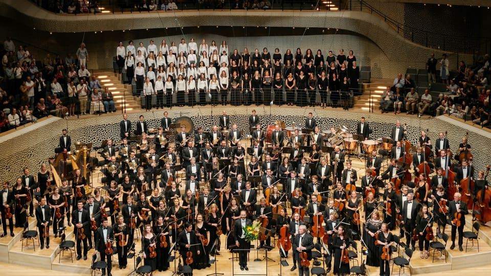 A full orchestra and choir on stage in a concert hall