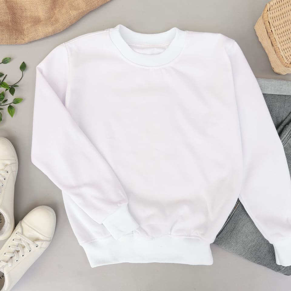 A plain white sweatshirt laid flat beside trainers