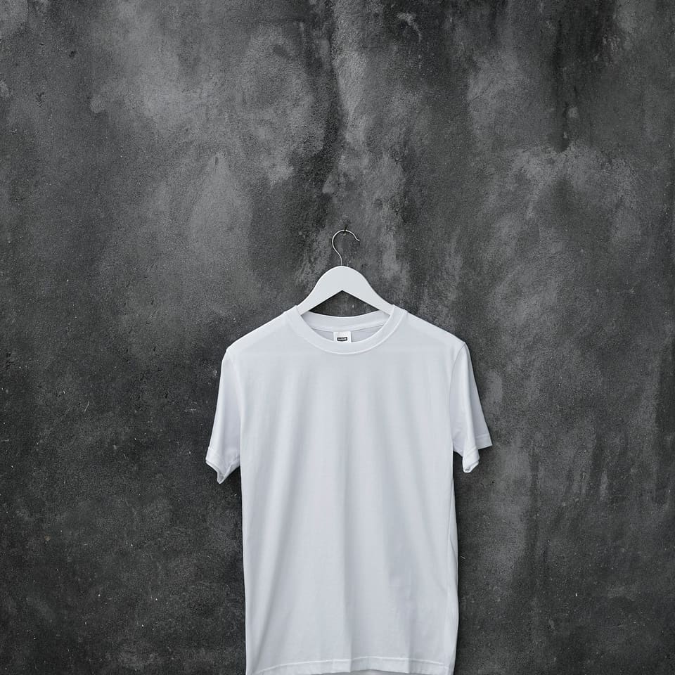 A plain white T-shirt on a hanger against a grey wall